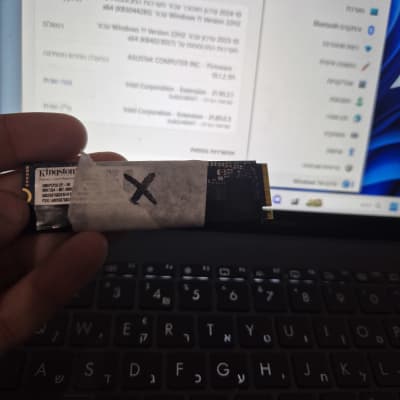 כונן SSD מוחזק מעל מקלדת מחשב נייד