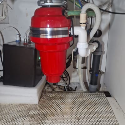 מטחנת אשפה אדומה מתחת לכיור עם צינורות חיבור