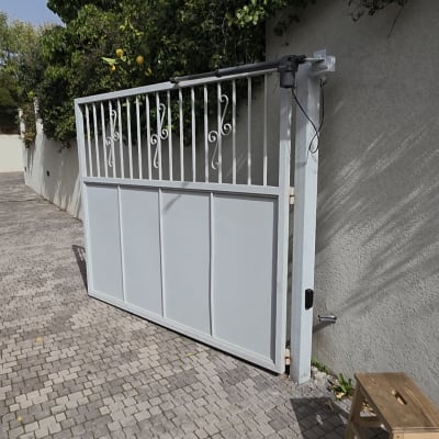 שער מתכת לבן בחניה עם צמחייה מסביב