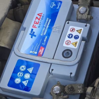 מצבר רכב עם תוויות אזהרה וחיבורים חשמליים