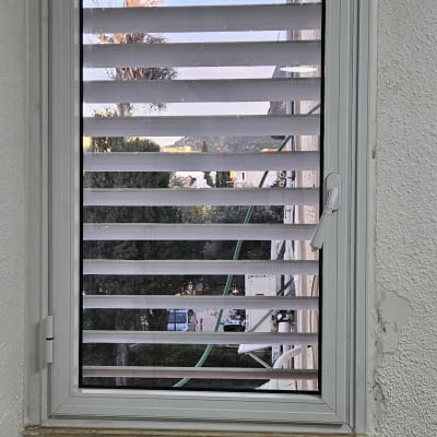 חלון עם תריסים מאלומיניום על קיר לבן