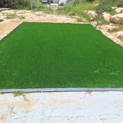 דשא סינתטי מותקן בחצר עם אבנים מסביב