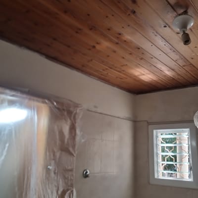 חדר בשיפוץ עם תקרה מעץ וחלונות מכוסים בניילון