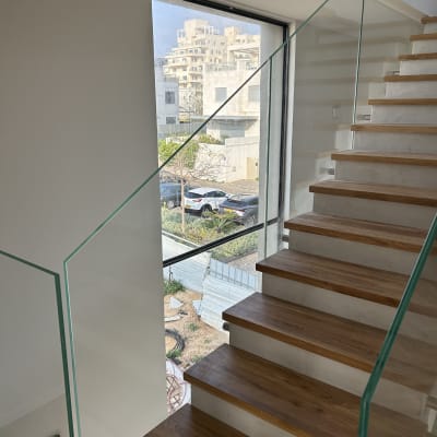 מדרגות עץ עם מעקה זכוכית ליד חלון גדול