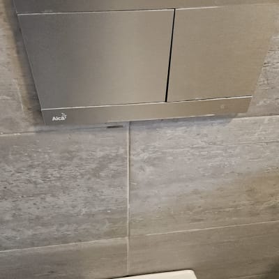 לחצן הדחה לאסלה על קיר אריחים אפור