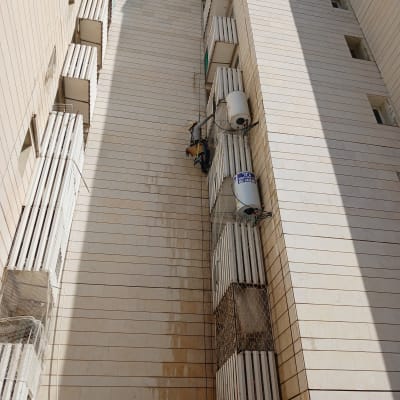 אדם תלוי על חבל ליד דודי שמש על קיר בניין