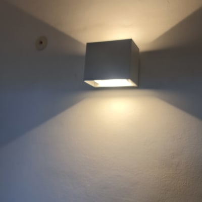 מנורת קיר מרובעת מוארת על קיר לבן