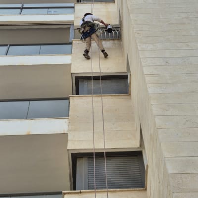אדם תלוי על חבלים מבצע עבודות גובה בבניין