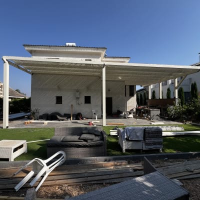 פרגולה לבנה בחצר עם ריהוט גן ודשא סינתטי