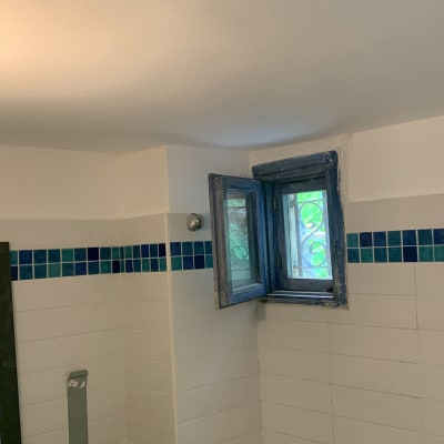 חלון עץ פתוח עם מסגרת כחולה בקיר אריחים לבנים