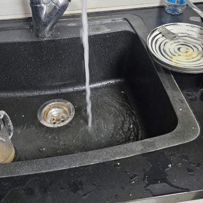 ברז מים זורם בכיור מטבח עם כלים מלוכלכים