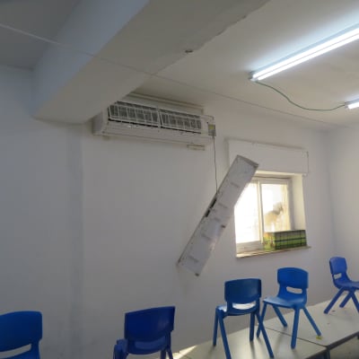 חדר עם מזגן תלוי וכיסאות כחולים על שולחנות