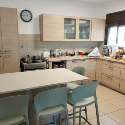 מטבח עם ארונות עץ, כיסאות ירוקים ושעון קיר