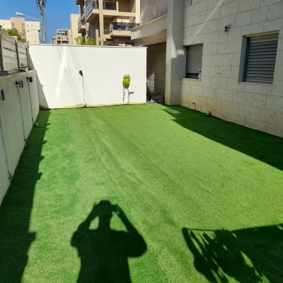 דשא סינתטי בחצר עם צינור השקיה על הקיר