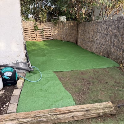 דשא סינתטי בחצר עם צינור השקיה וגדר במבוק