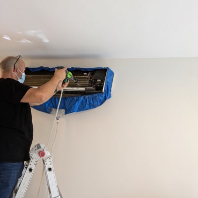 טכנאי מתקין מזגן על קיר בעזרת סולם