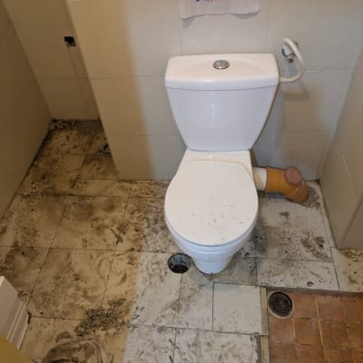 שירותים עם רצפה מלוכלכת וחור פתוח בצנרת