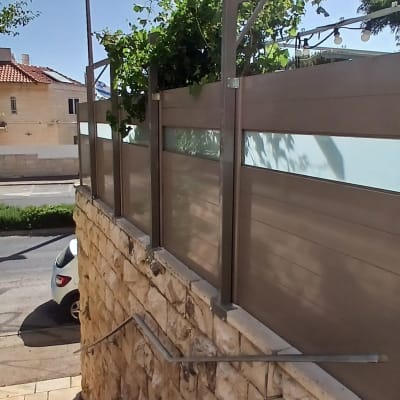 גדר מתכת עם לוחות זכוכית ושיחים ירוקים