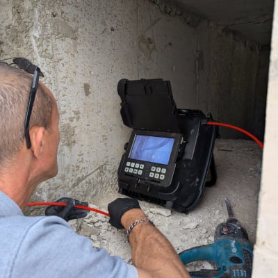 אדם משתמש במכשיר לאיתור נזילות בקיר בטון