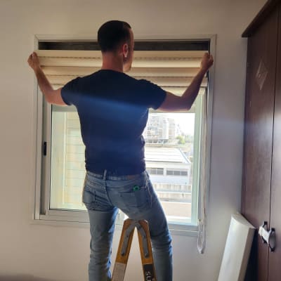 אדם מתקין תריסים על חלון בעזרת סולם