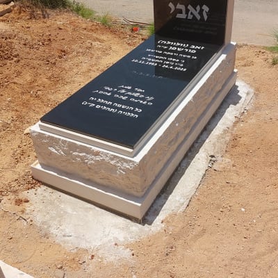 מצבה שחורה עם כיתוב לבן בבית קברות