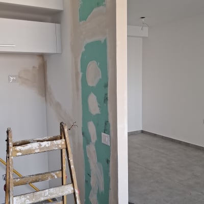 קיר עם טיח ירוק וסולם בעבודת שיפוץ