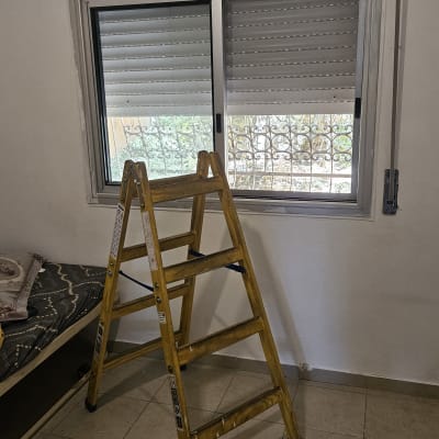 סולם מול חלון עם תריסים סגורים למחצה