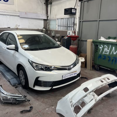 רכב לבן במוסך עם פגוש מפורק על הרצפה