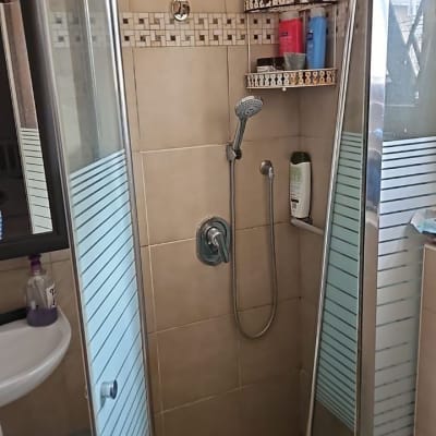 תא מקלחת עם דלתות זכוכית ומדף מוצרי טיפוח