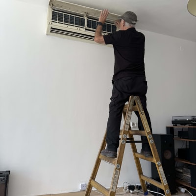 אדם על סולם מתקן מזגן על קיר