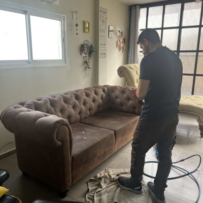 אדם מנקה ספה חומה עם שואב אבק