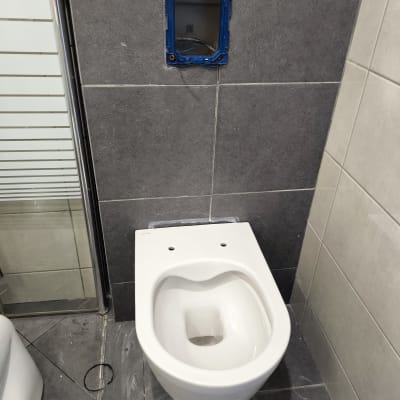 אסלה מותקנת בחדר אמבטיה עם קיר אריחים אפור