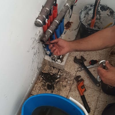 אינסטלטור עובד על צינורות עם כלים ודלי