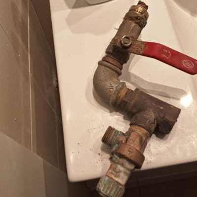 ברז מתכת עם ידית אדומה על כיור לבן