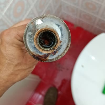 יד מחזיקה צינור חלוד בחדר אמבטיה עם רצפה אדומה