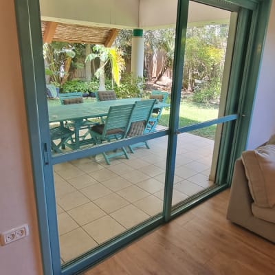 דלת זכוכית עם מסגרת ירוקה נפתחת לחצר עם שולחן וכיסאות