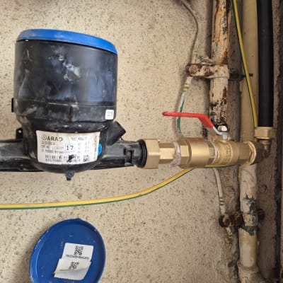 מונה מים עם ברז אדום וצינורות מחוברים