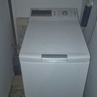 מכונת כביסה בחדר כביסה עם מוצרי ניקוי על מדף