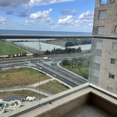 מעקה זכוכית במרפסת עם נוף לים ולבניין סמוך