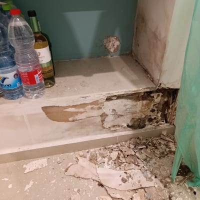 קיר עם קילופי צבע ונזק, בקבוקי מים ויין על מדף