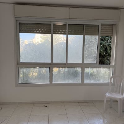 חלון גדול עם תריסים וכיסא פלסטיק לבן בחדר ריק