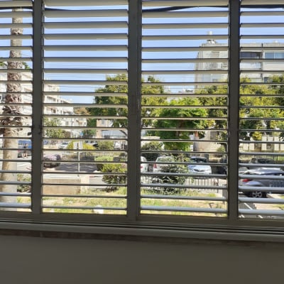 תריסים אופקיים פתוחים עם נוף חיצוני של עצים ומכוניות