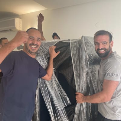 צוות מובילים מחייך לצד ציוד עטוף בשמיכות וסטרץ