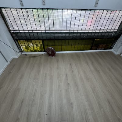 רצפת פרקט עם מאוורר קטן ליד חלון סורג.