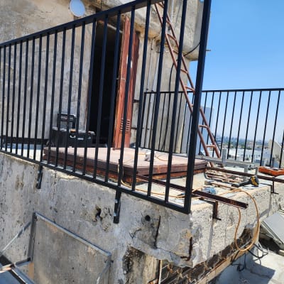 מעקה מתכת שחור מותקן על מרפסת בטון ישנה