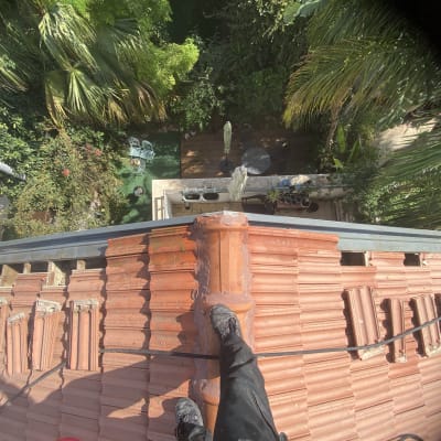 אדם עומד על גג רעפים אדום עם צינור שחור