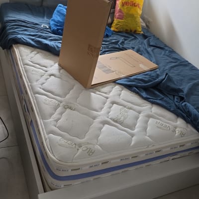 מיטה עם מזרן, קרטון ושקית על מצעים כחולים