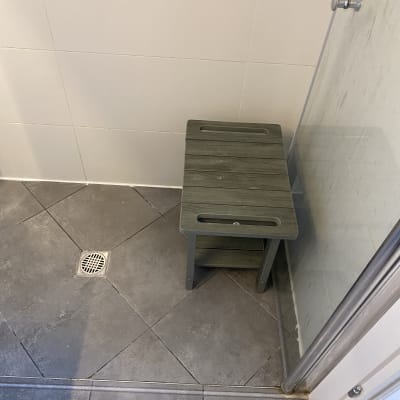 מושב עץ במקלחת עם רצפת אריחים וניקוז