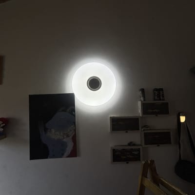 מנורה עגולה מוארת על קיר עם מדפים ותמונה