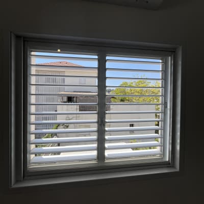 חלון עם תריסים ונוף חיצוני של בניינים ועצים